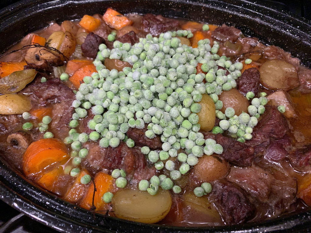 adding frozen peas to mostly cooked stew in roasting pan