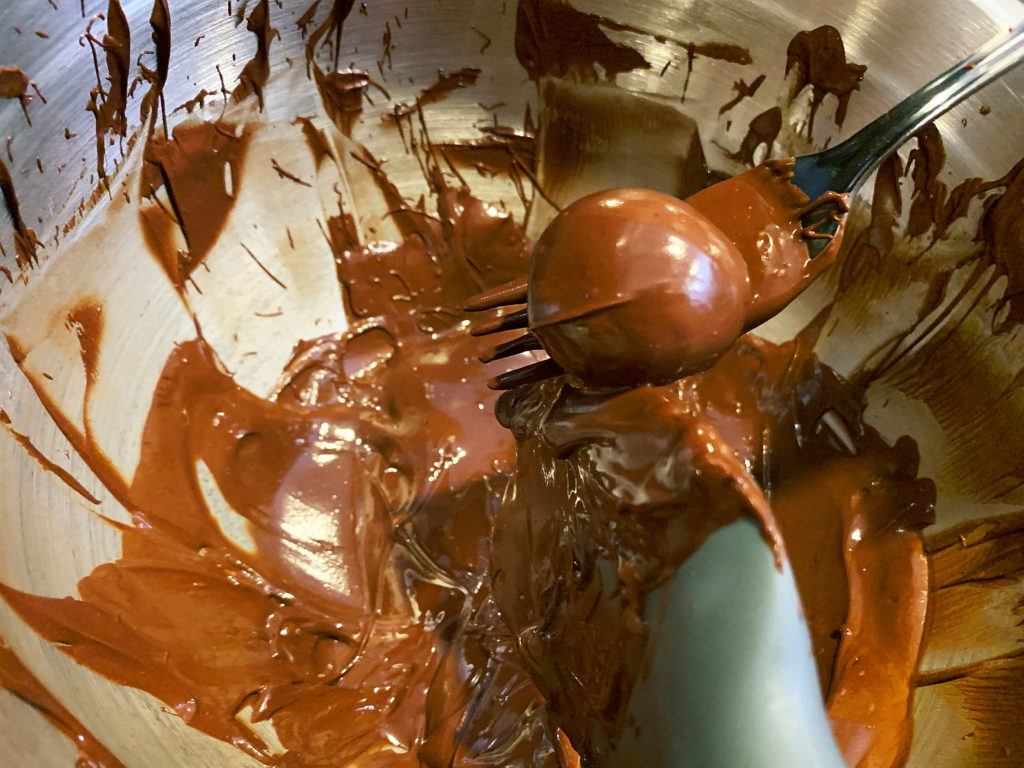 using a fork to dip a bourbon ball in melted chocolate