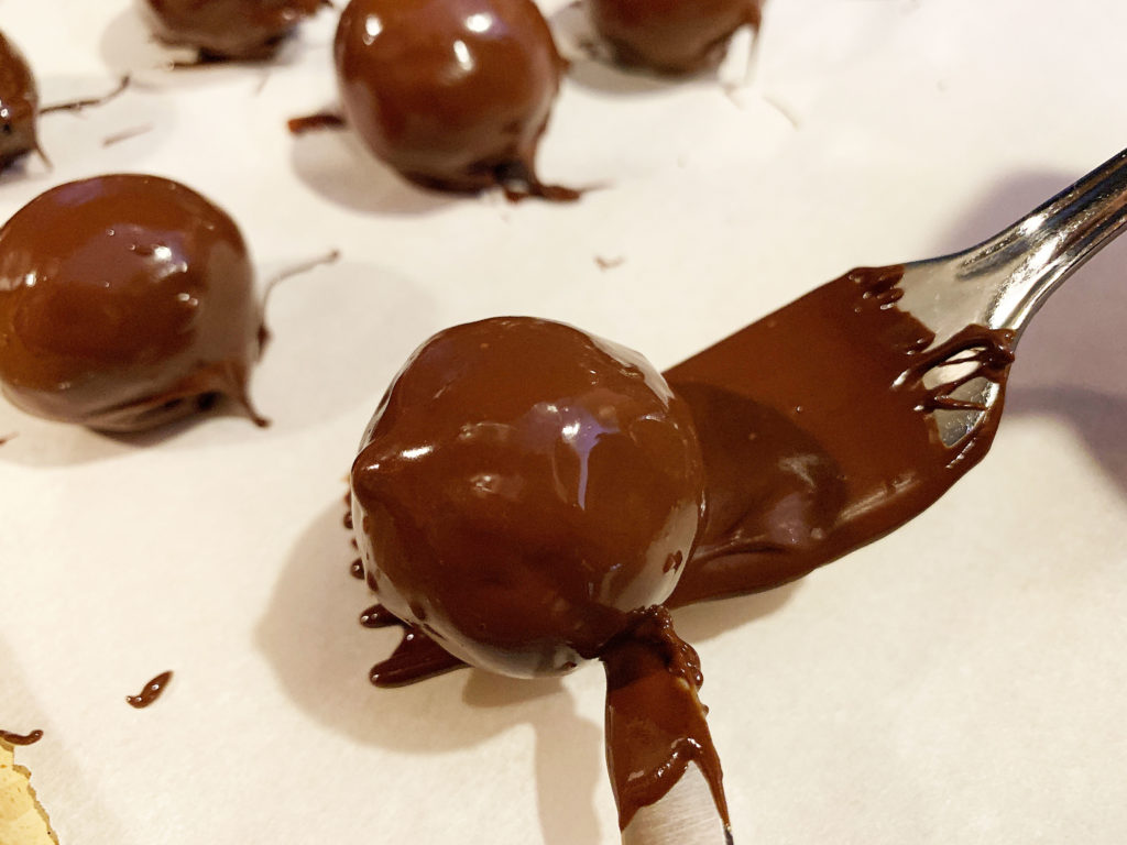 pushing chocolate covered bourbon ball off of fork onto parchment paper