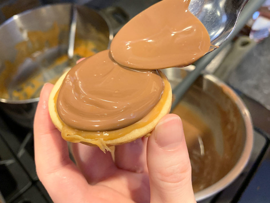 spreading chocolate onto the caramel covered cookies