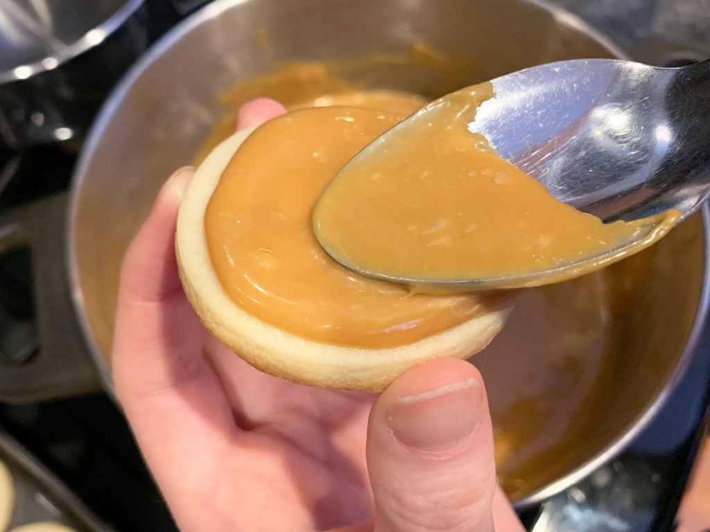 spreading the caramel onto the cookie with the back of a spoon