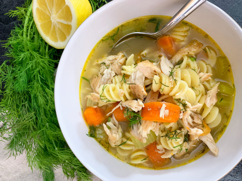 bowl of chicken noodle soup with lemon and fresh dill on the side