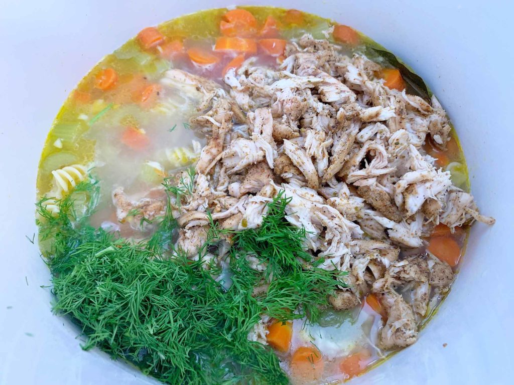 adding shredded chicken and fresh dill to the chicken noodle soup