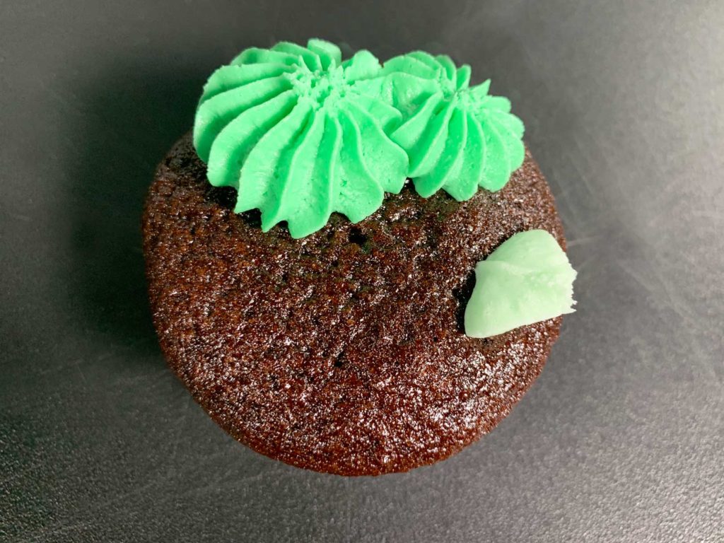 piping buttercream cactus on top of cupcake
