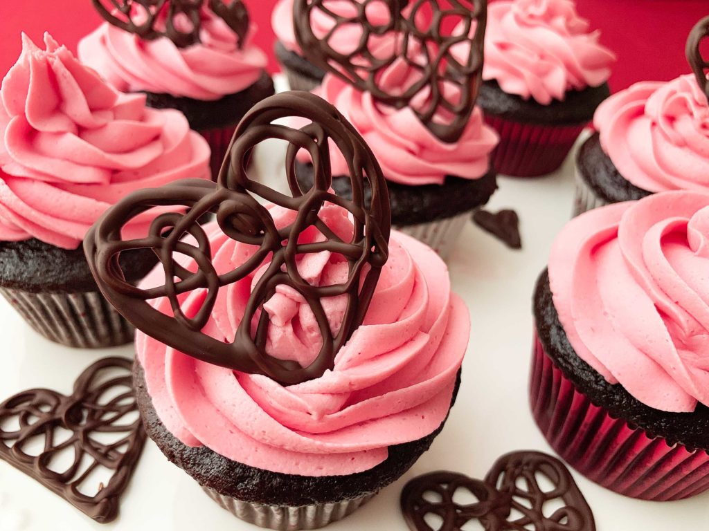 Close up of chocolate cupcakes with raspberry buttercream, with a decorate chocolate heart on top