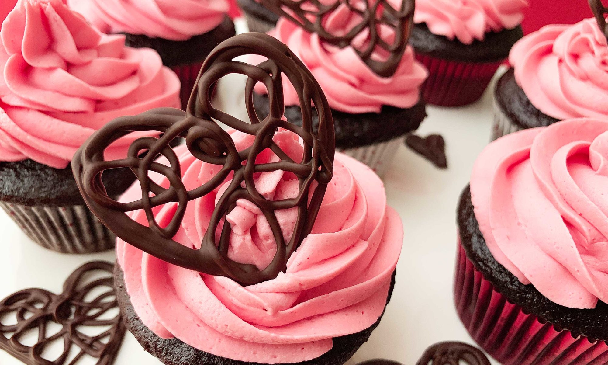 Close up of chocolate cupcakes with raspberry buttercream, with a decorate chocolate heart on top