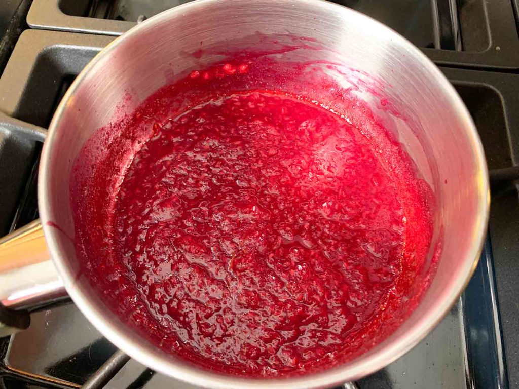 Raspberries mashed up and heating in a small saucepan