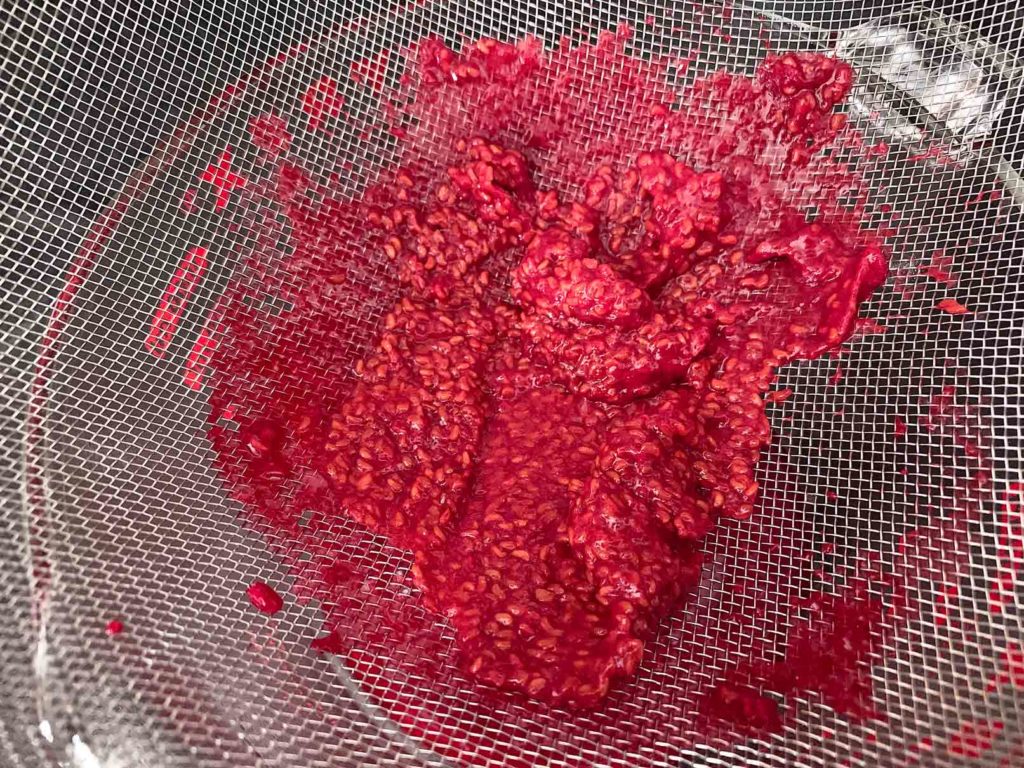 Pressing raspberries through a sieve to get rid of the seeds