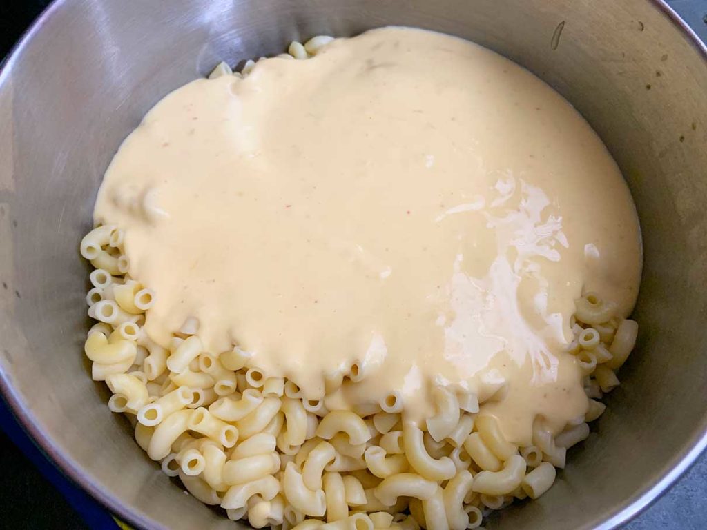 pouring the cheese sauce into a pot full of cooked macaroni pasta