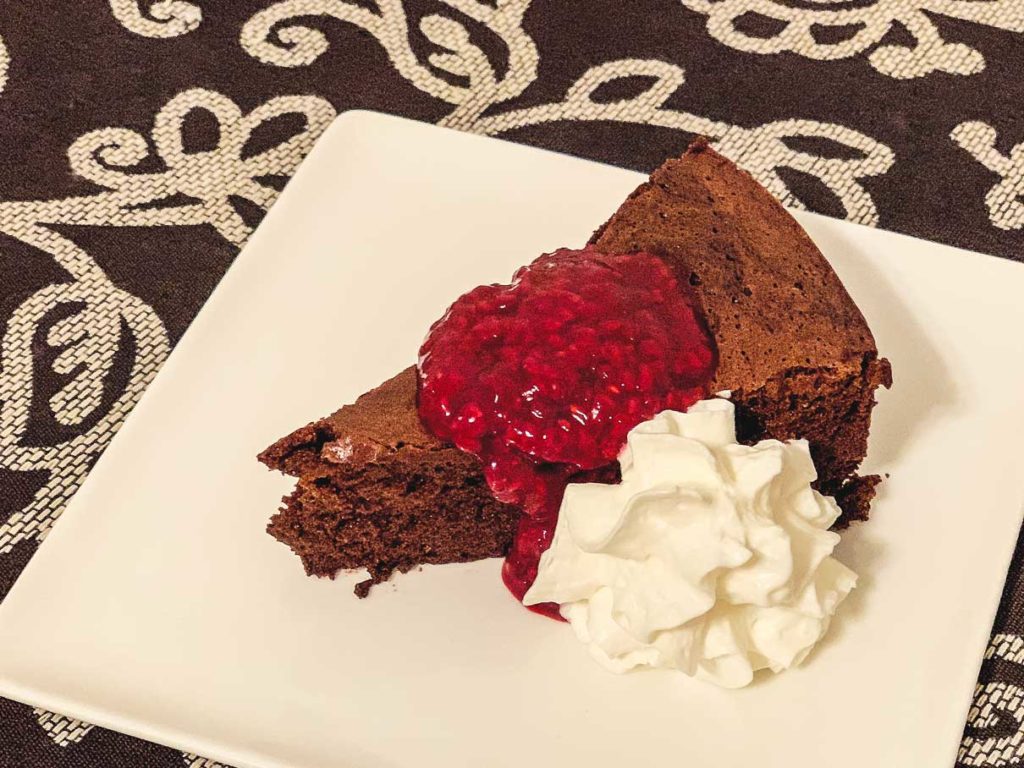 piece of flourless chocolate cake on a plate with raspberry sauce and whipped cream
