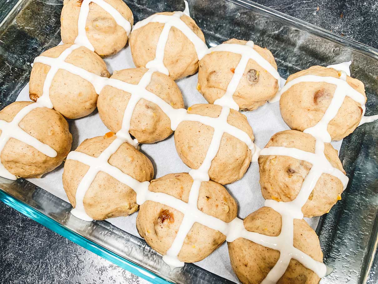 piping a cross on top of the risen dough buns