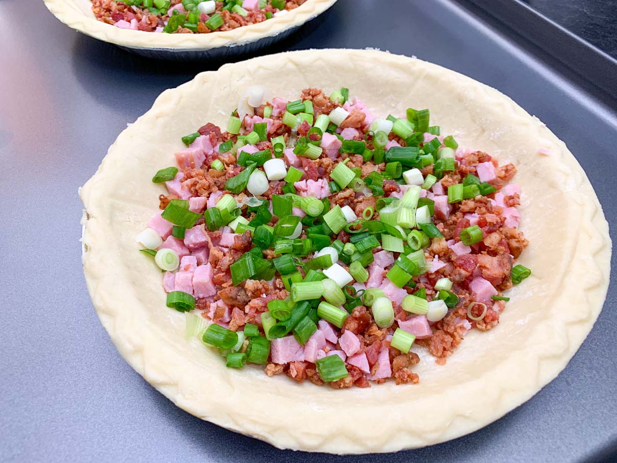 ham, bacon and green onion sprinkled on bottom of pie shell