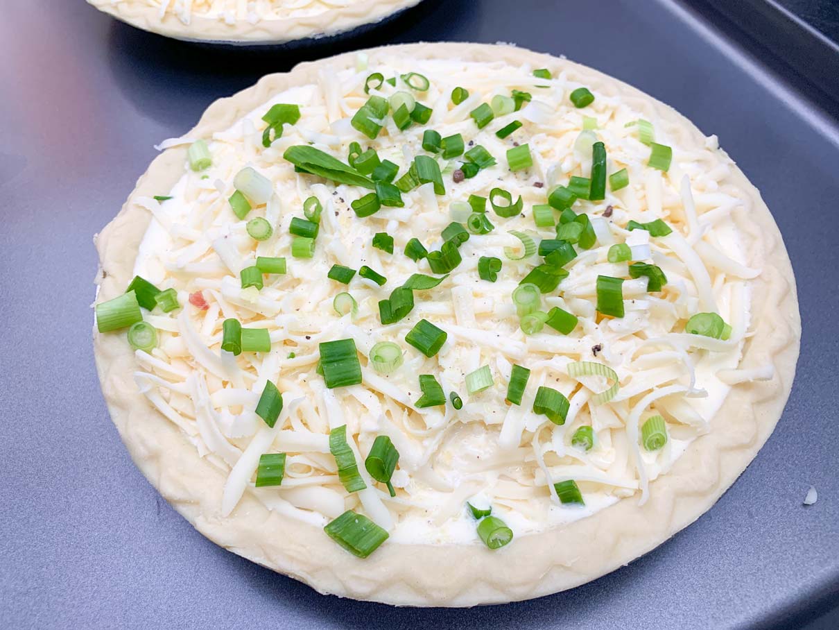 quiche, ready for oven, with green onion sprinkled on top