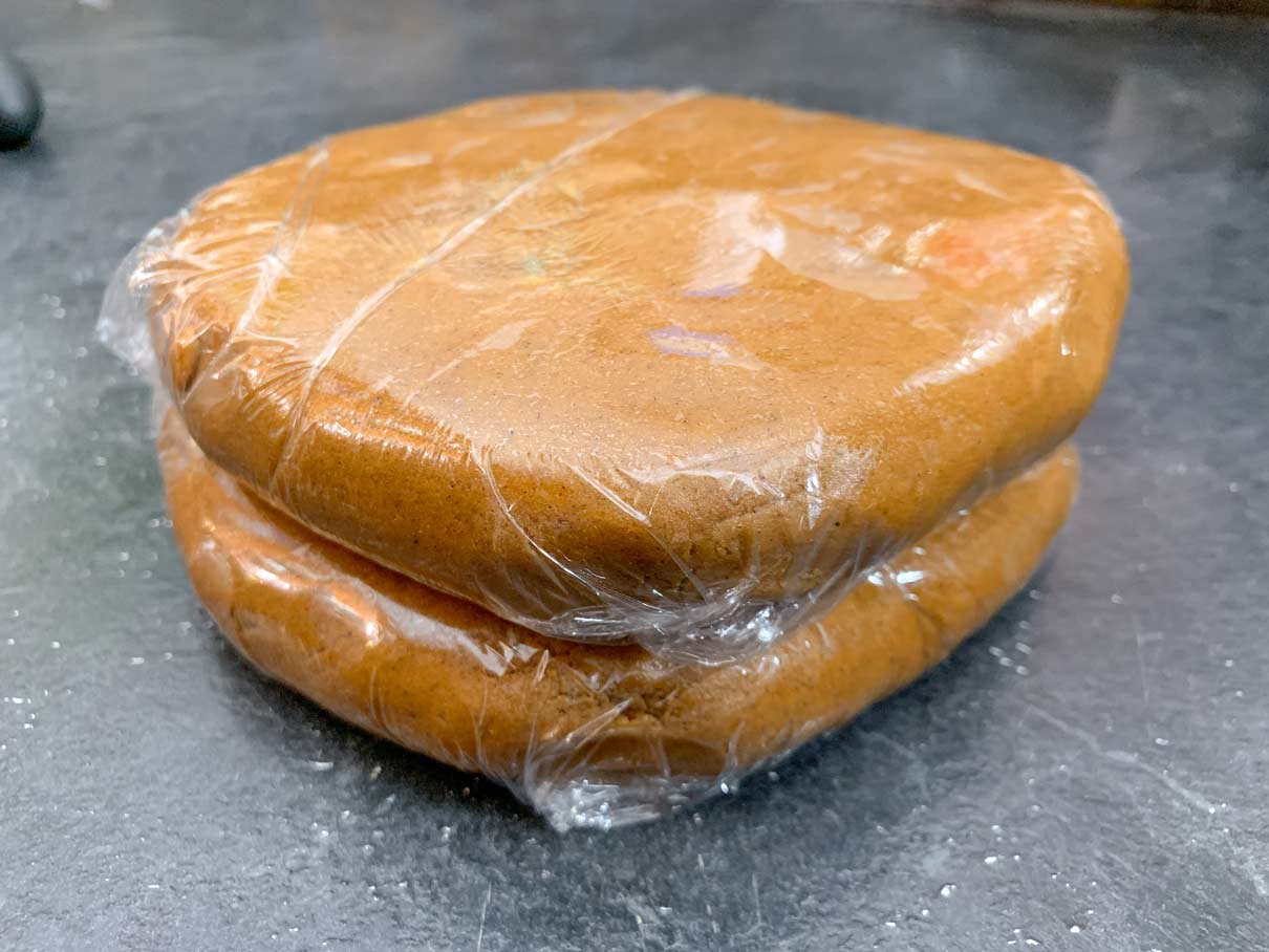two discs of gingerbread dough, wrapped in plastic wrap, ready to go in fridge