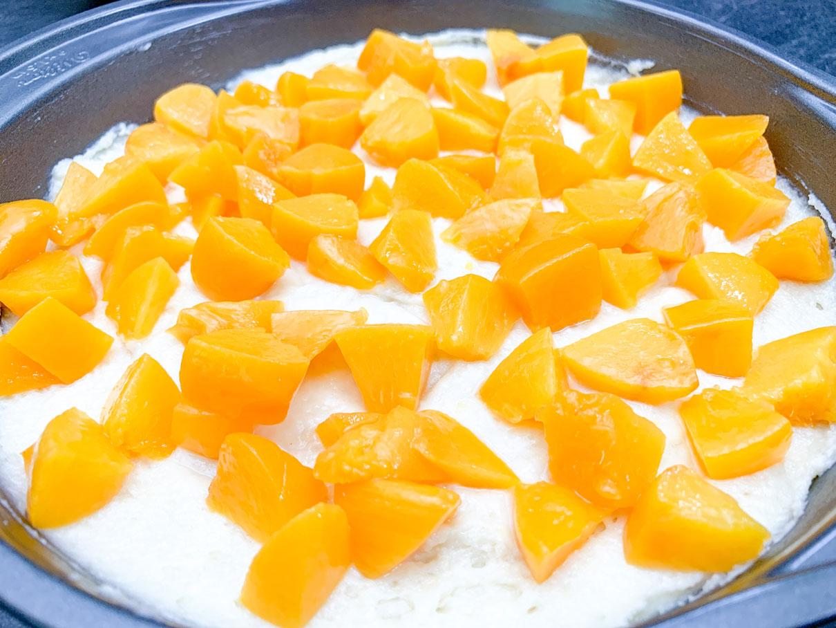 close up of chopped up peaches on top of cake batter