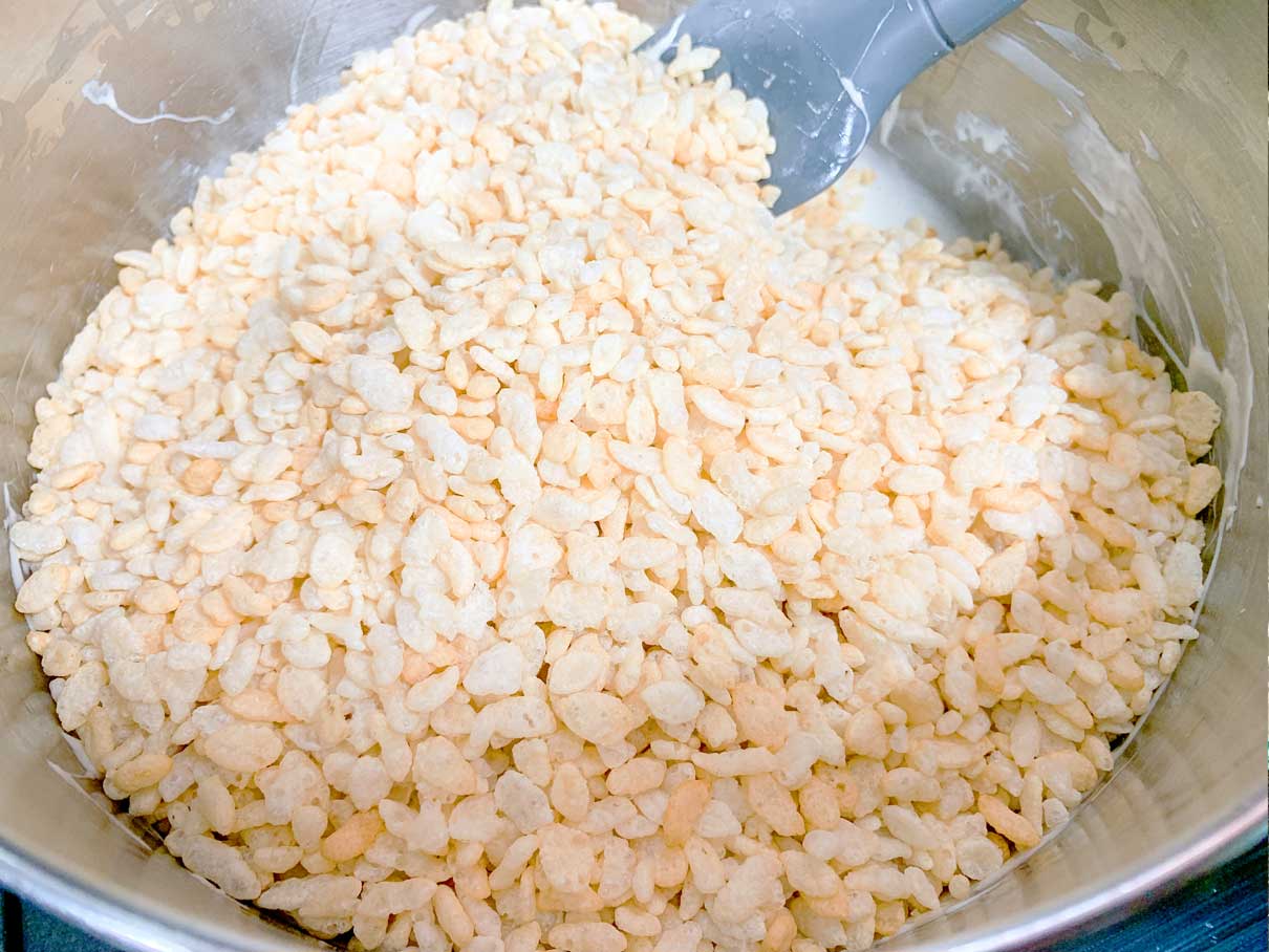 rice krispies poured on top of melted marshmallows in a saucepan