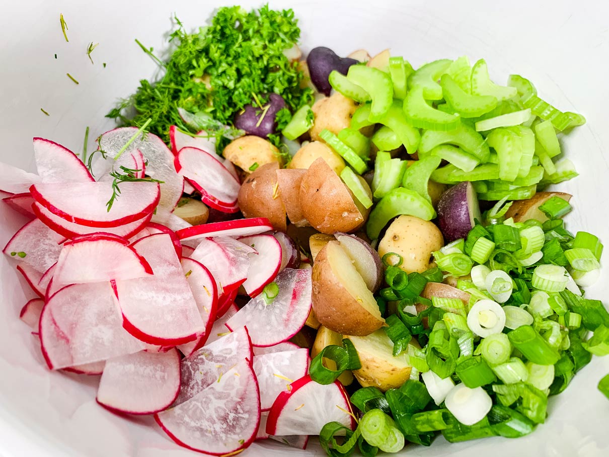 bowl full of chopped up potatoes, celery, radishes, spring onion and herbs