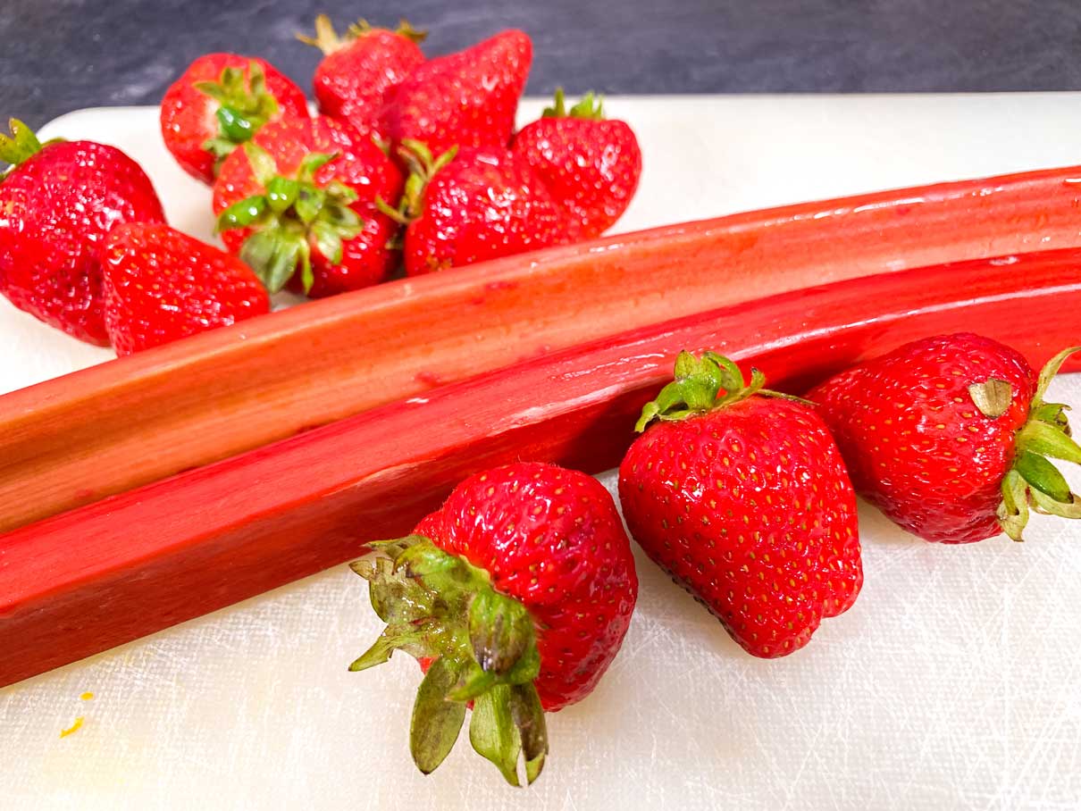 strawberries and rhubarb sticks on a cutting board