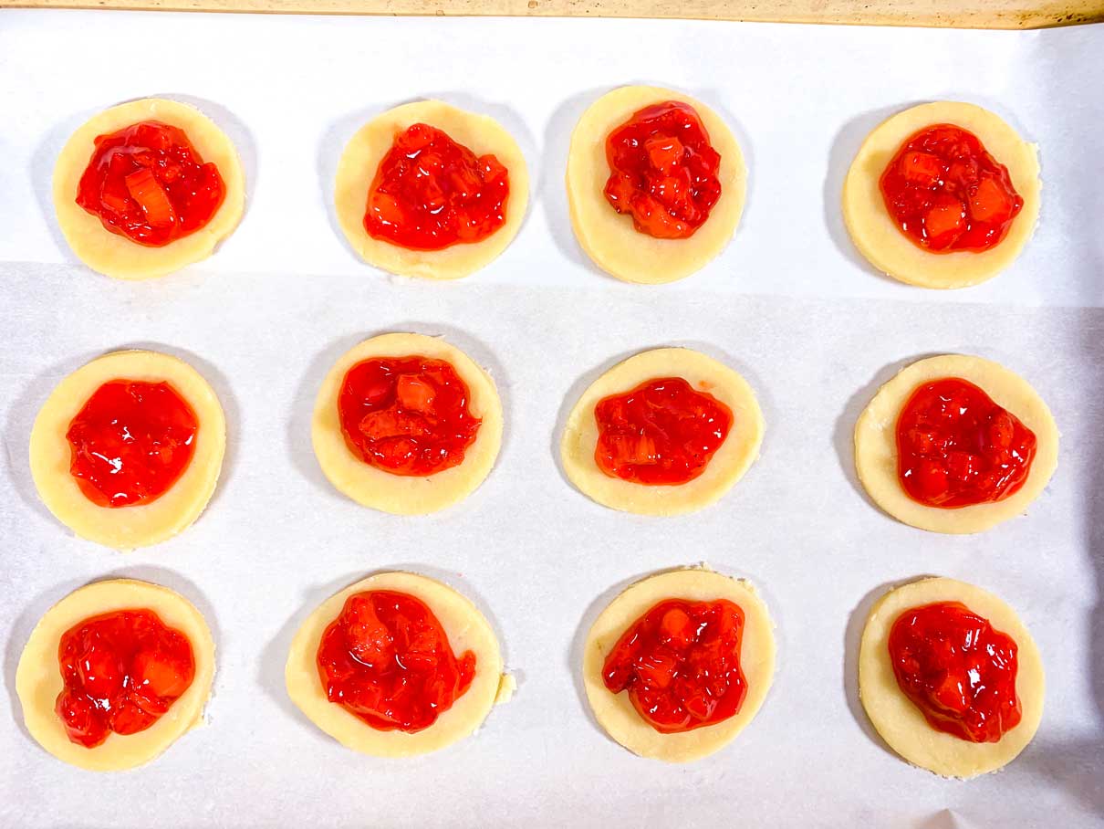 dough circles on a parchment lined cookie tray, with a spoonful of filling on each