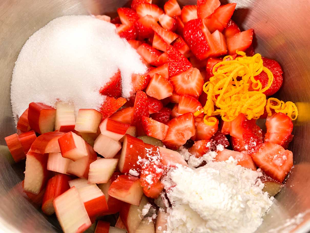 chopped up strawberries and rhubarb in a saucepan with sugar, cornstarch and orange zest