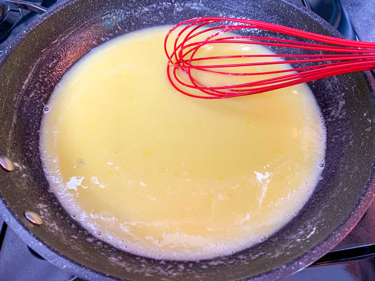 lemon curd ingredients all whisked together in a frying pan, cooking