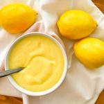 overhead image of a bowl of lemon curd with lemons beside it