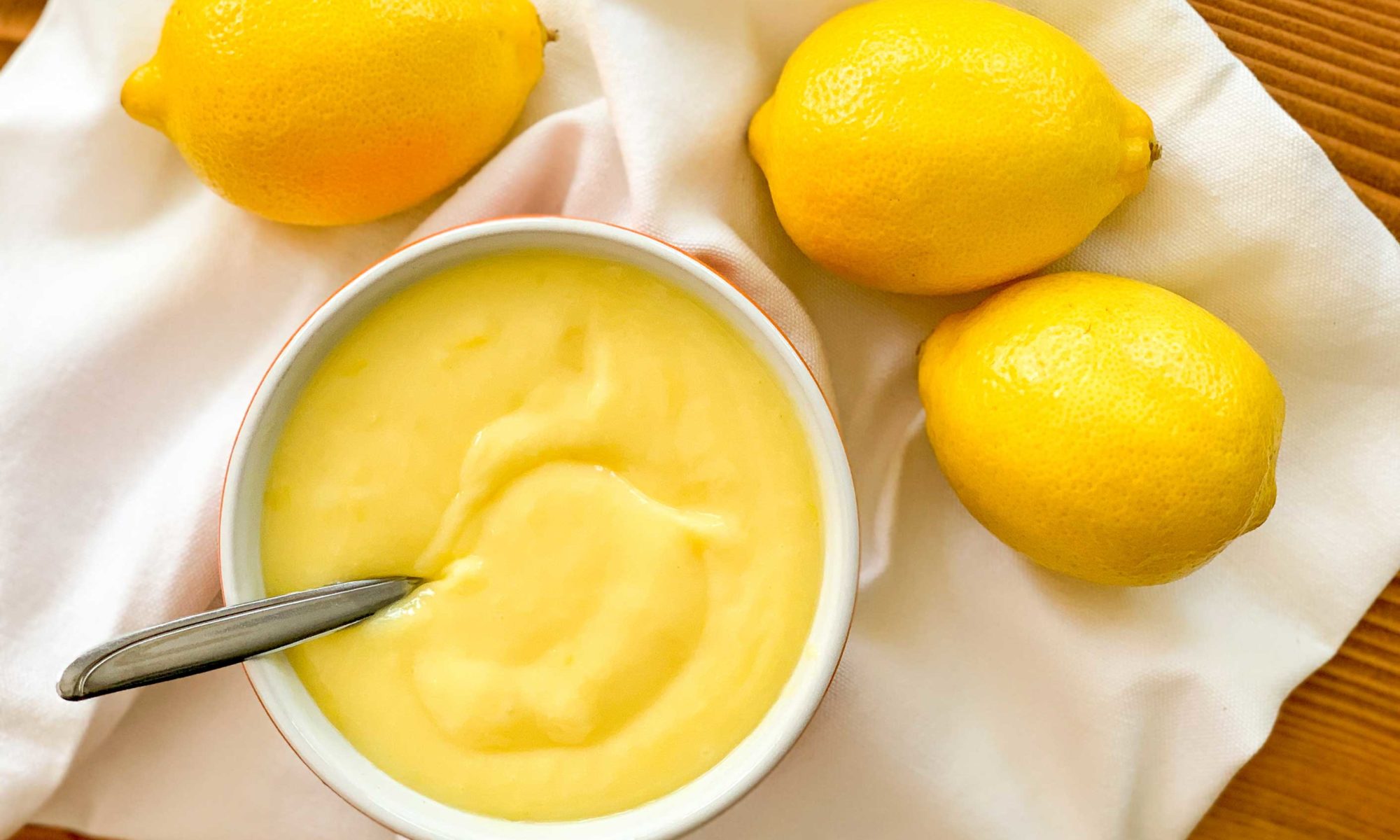 overhead image of a bowl of lemon curd with lemons beside it