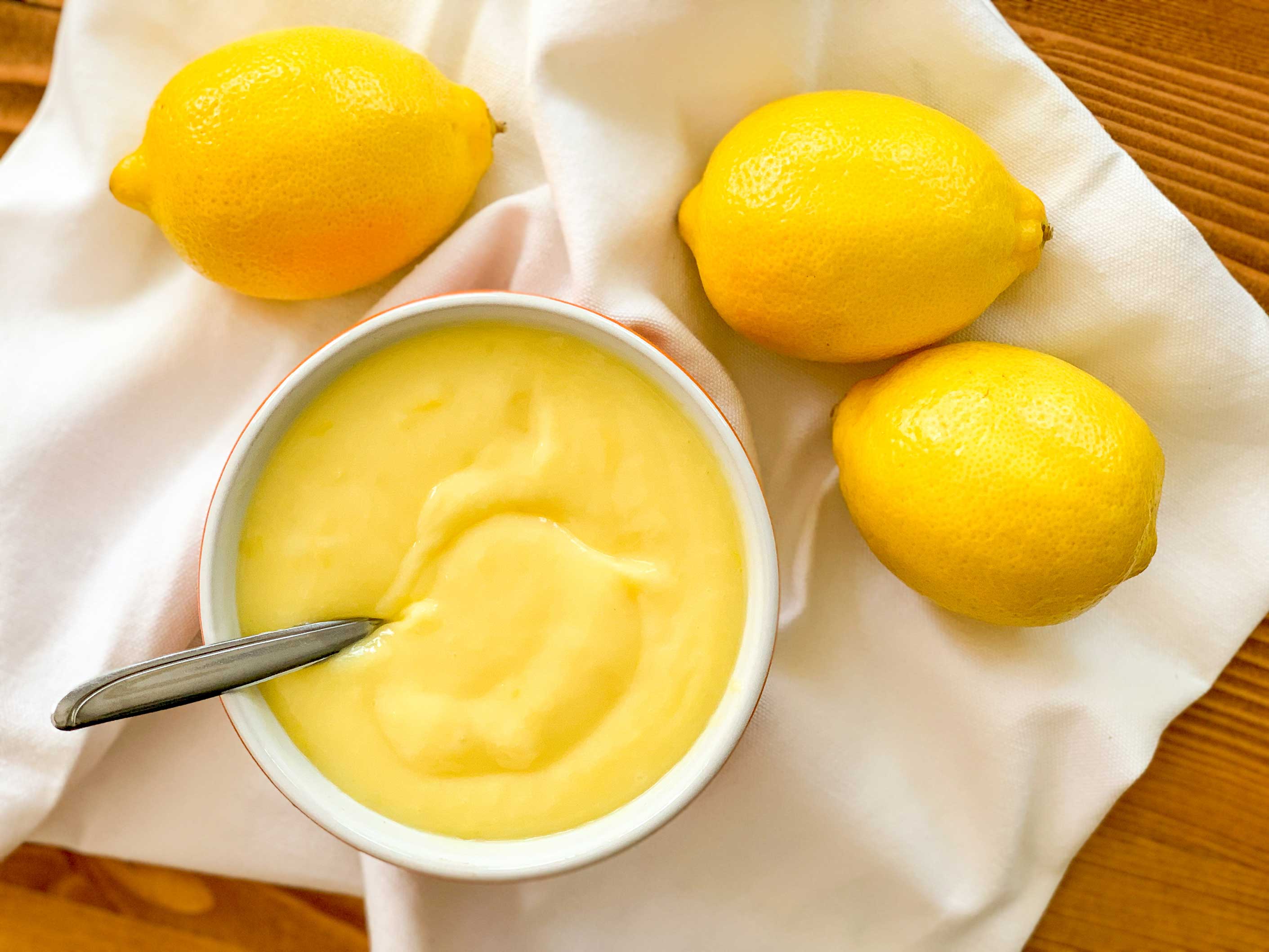 overhead image of a bowl of lemon curd with lemons beside it