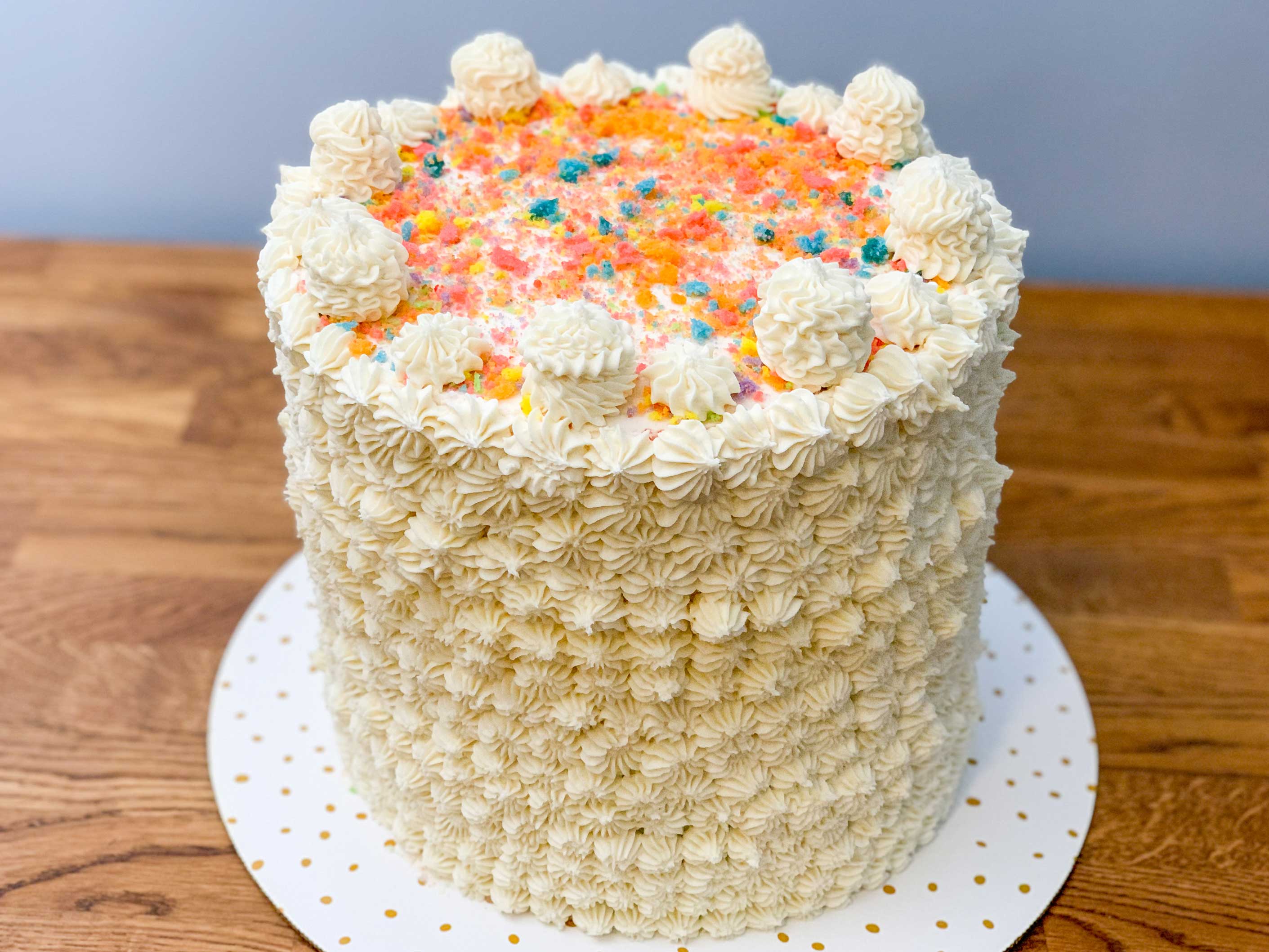 finished cake covered in white buttercream frosting, and rainbow cake crumbs sprinkled on top