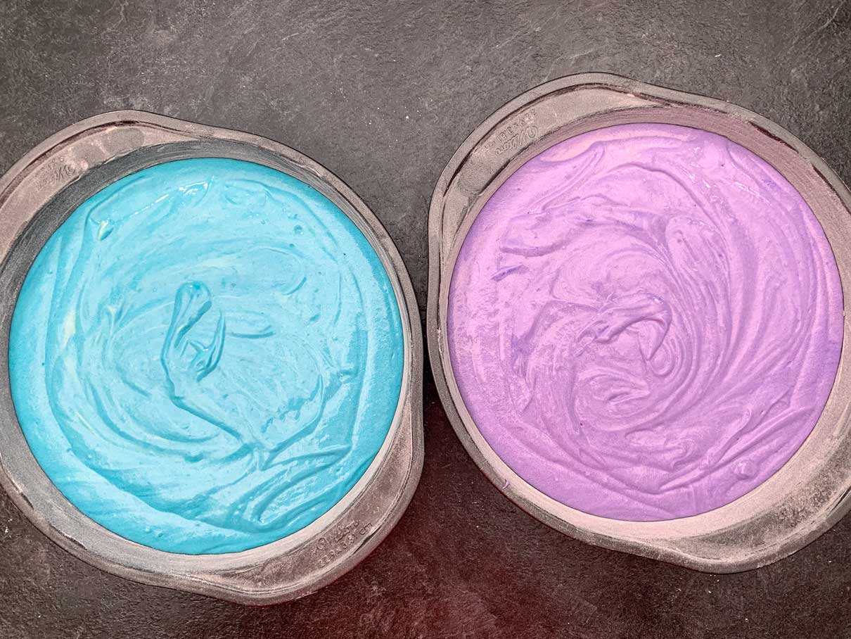 two nine inch round baking pans, one filled with blue batter, one filled with purple batter