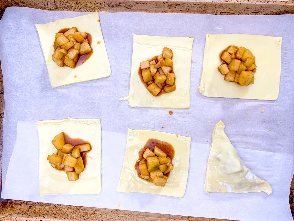 squares of puff pastry on a baking tray, with a spoonful of apple filling on top of each