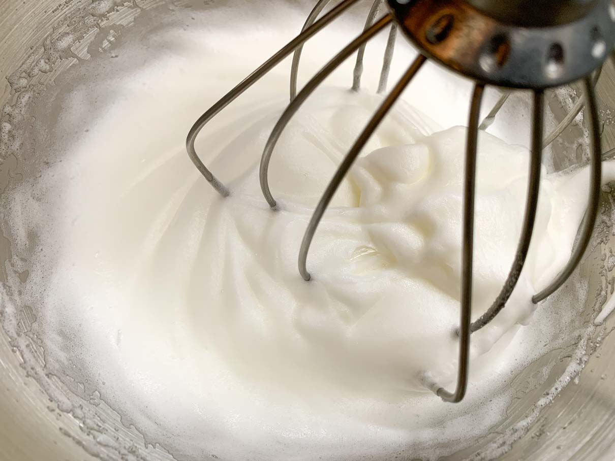 Whipping egg whites with sugar until medium-stiff peaks are formed