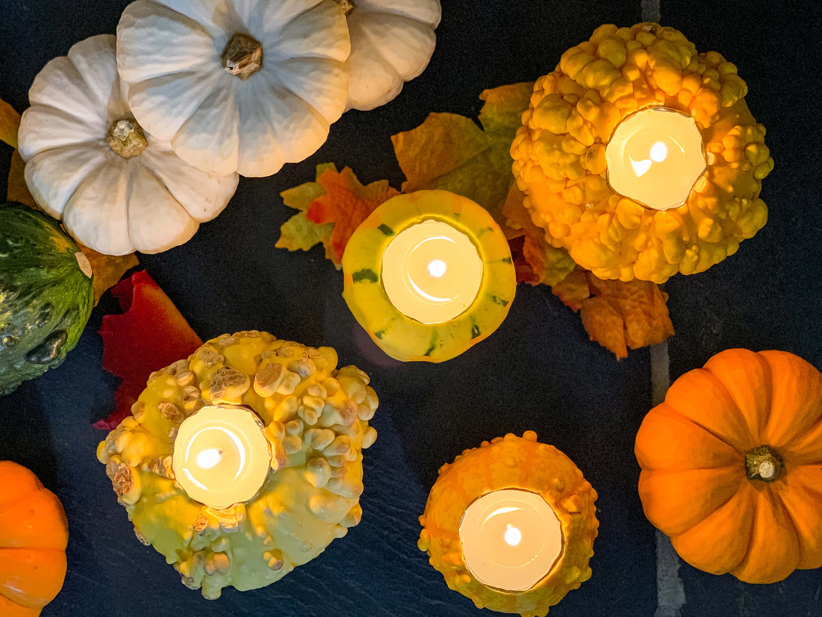 overhead shot of gourds with tea lights lit, surrounded by fall leaves and mini pumpkins