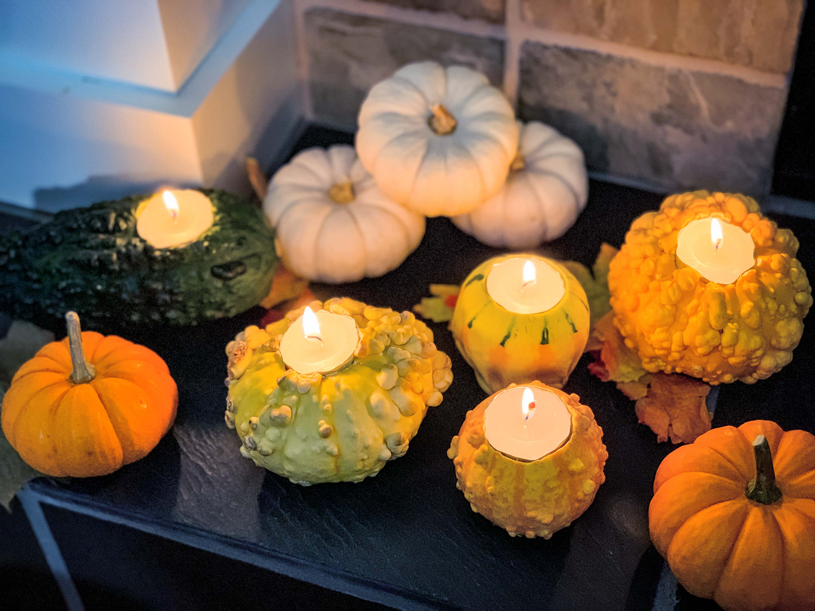 fall gourds with tea lights lit, sitting on the mantle of a fireplace