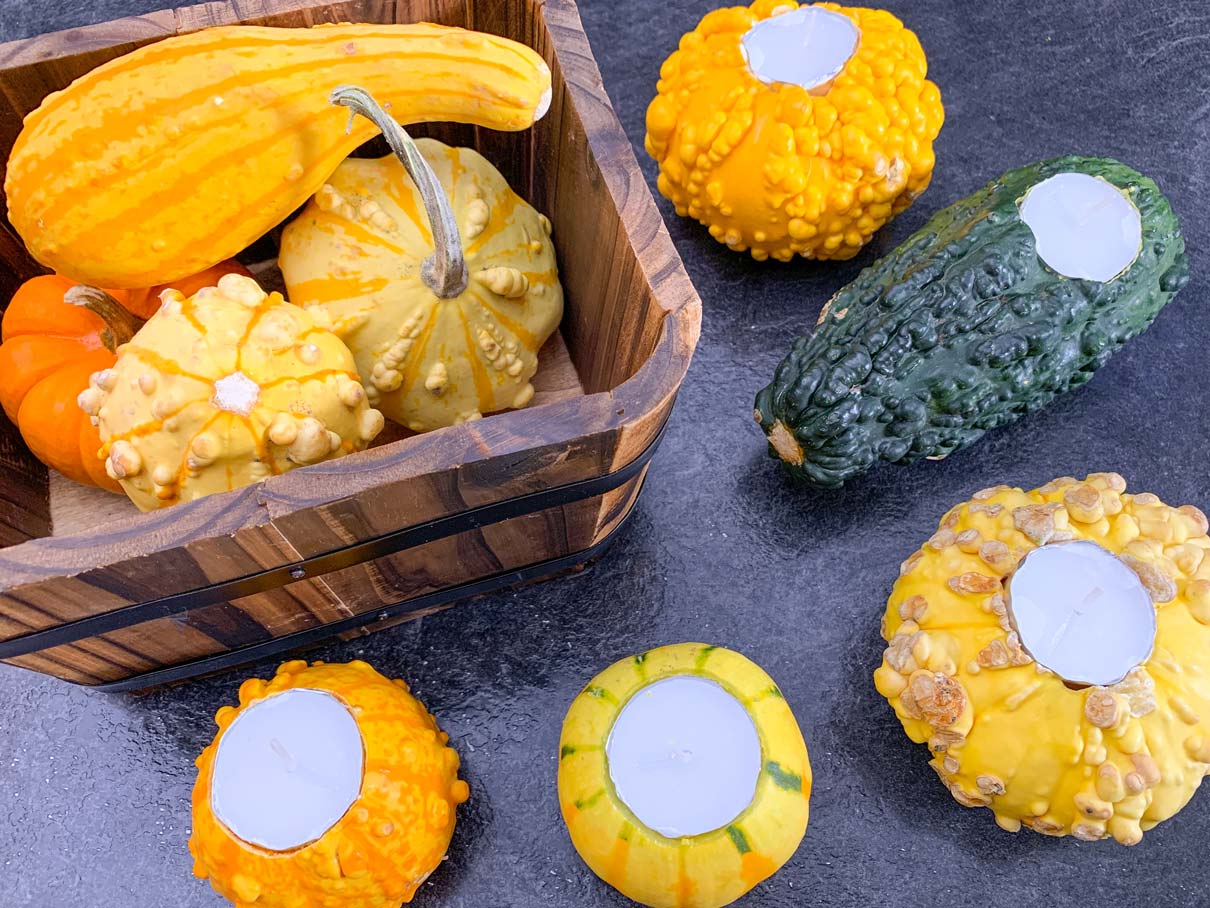 five gourds with tealights in them, sitting on the counter next to a basket of gourds