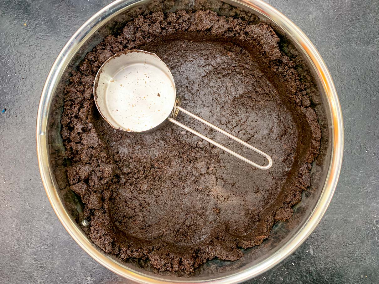Pressing the crumbs into the springform pan with the back of a measuring cup