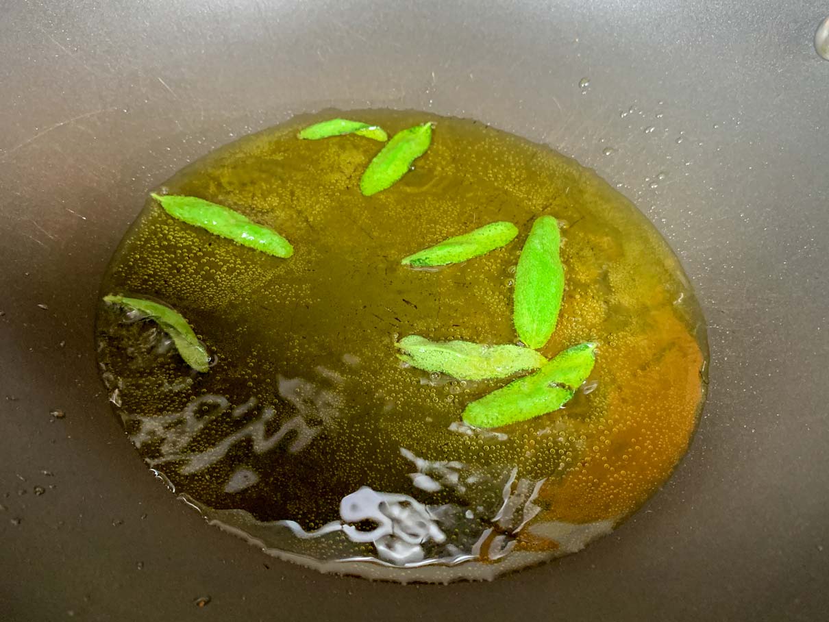 A thin layer of oil in a pan with sage leaves frying in it