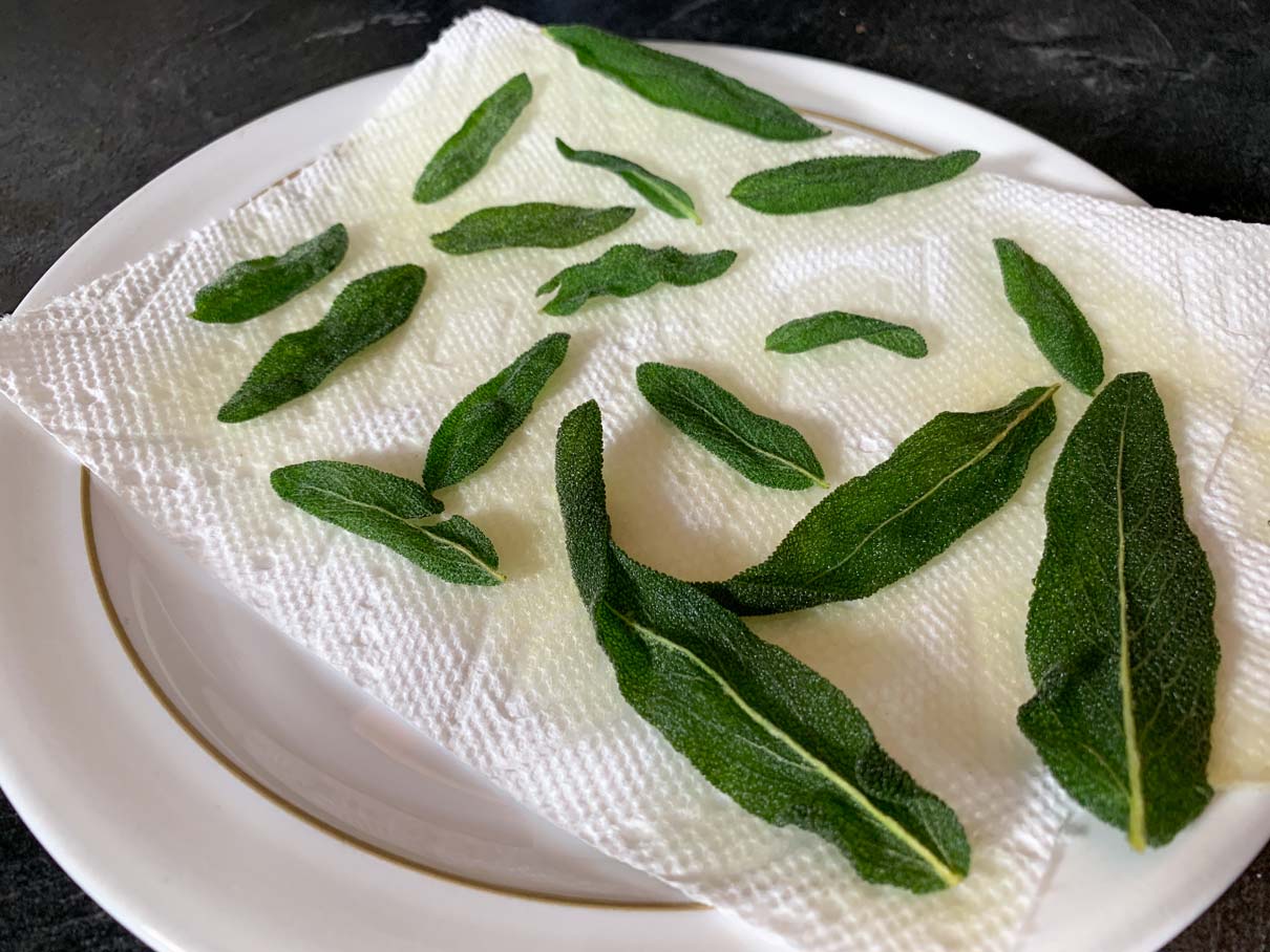 The crispy fried sage leaves cooling on a piece of paper towel