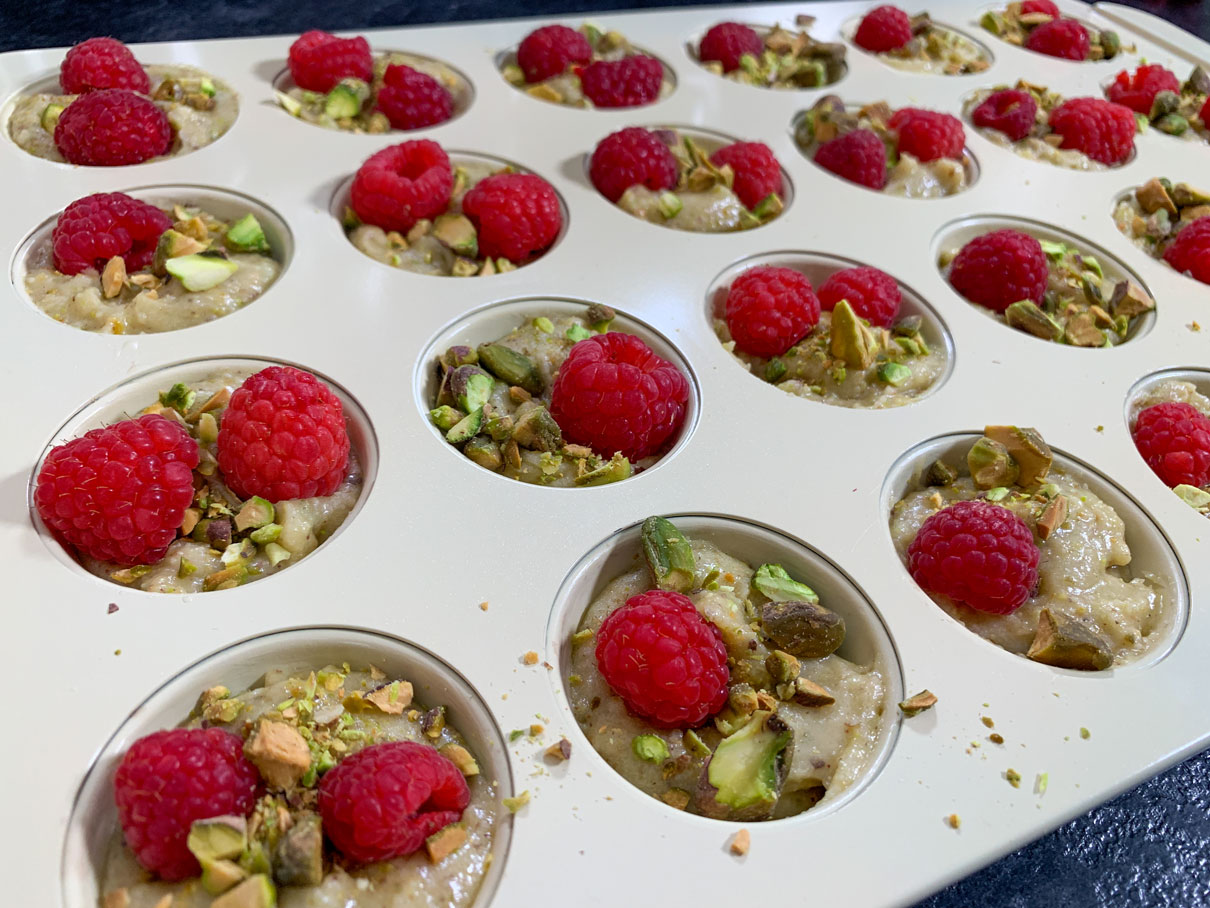 Close up of cupcake tin with raspberries and pistachios sprinkled on top of the batter