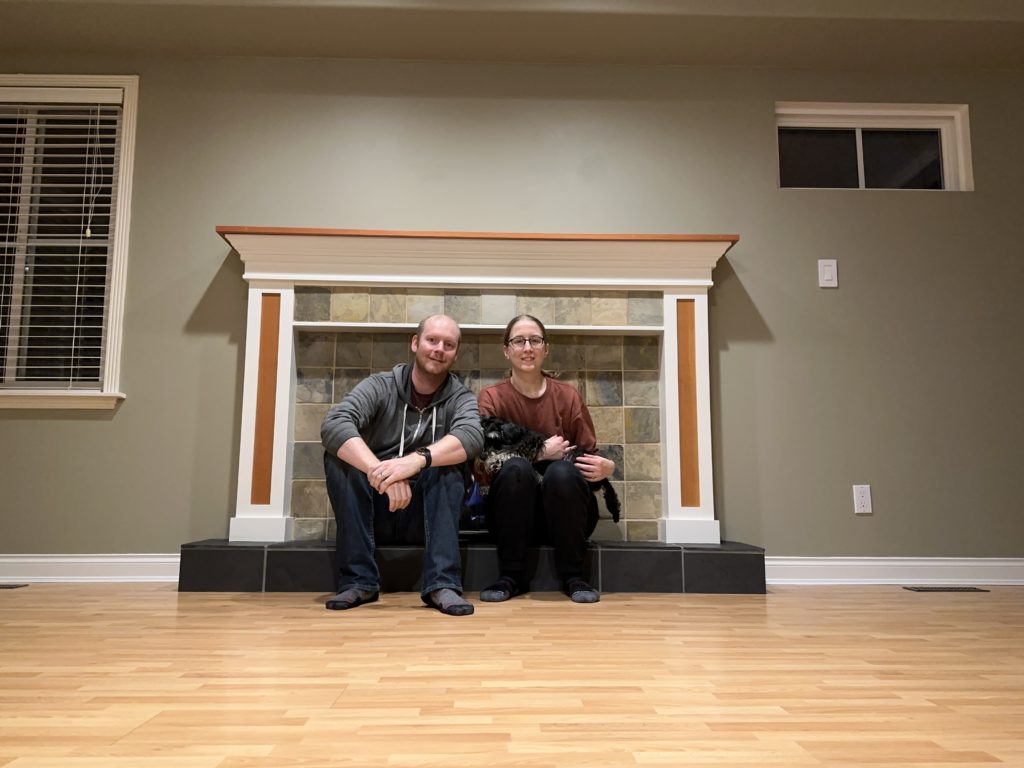 Collin and Joan sitting in front of their fireplace in an empty living room on moving day.