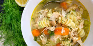 bowl of chicken noodle soup with lemon and fresh dill on the side