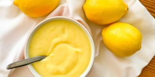 overhead image of a bowl of lemon curd with lemons beside it