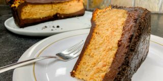 Close up of a slice of cheesecake on it's side, on a plate, with the rest of the cheesecake in the background